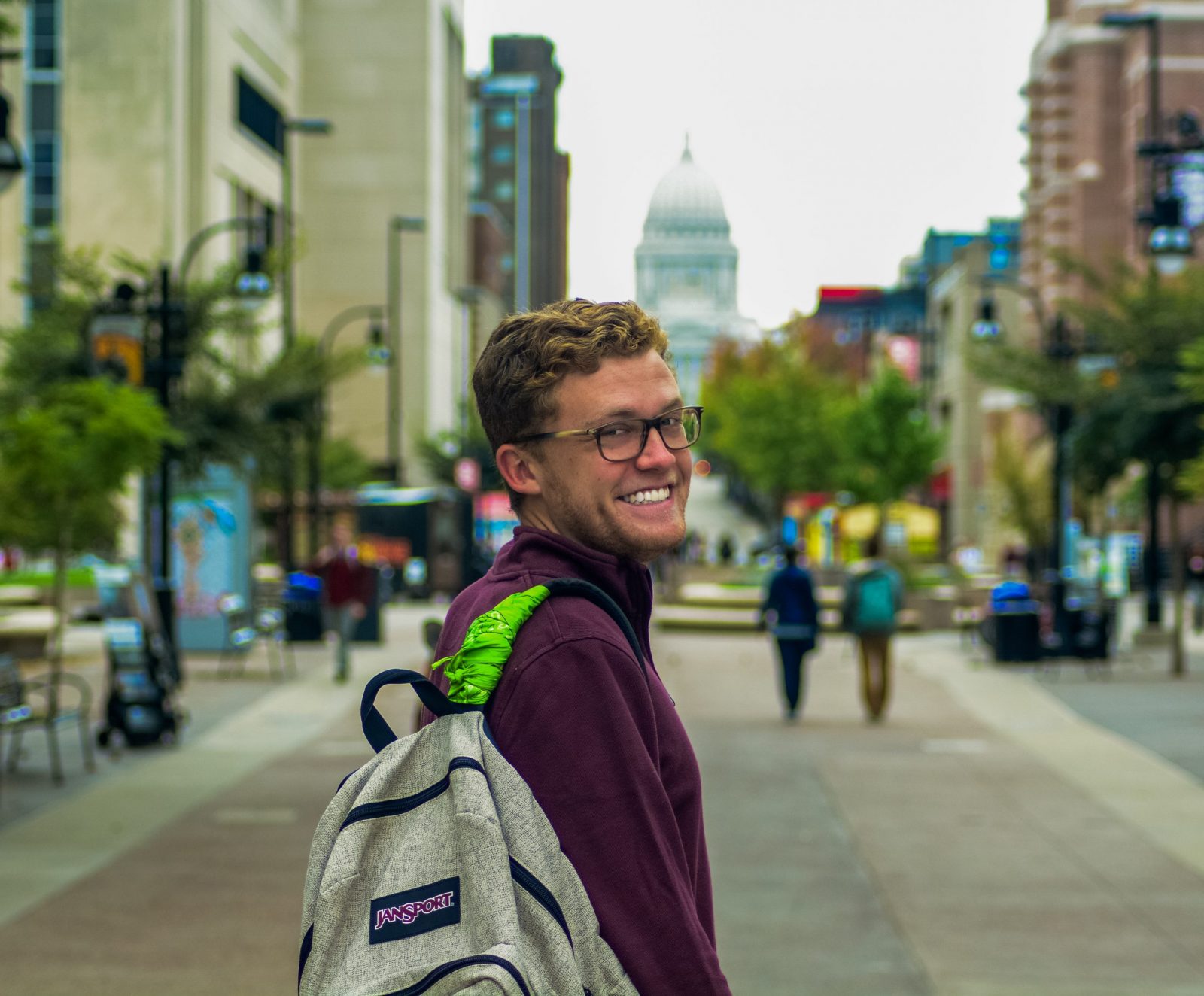 Student Colin Bass stands at the base of State Street, the capitol behind him in the distance, his backpack strap wrapped with a green bandana.