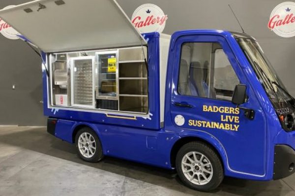 A blue electric vehicle food truck with 'Badgers Live Sustainably' written on the side.